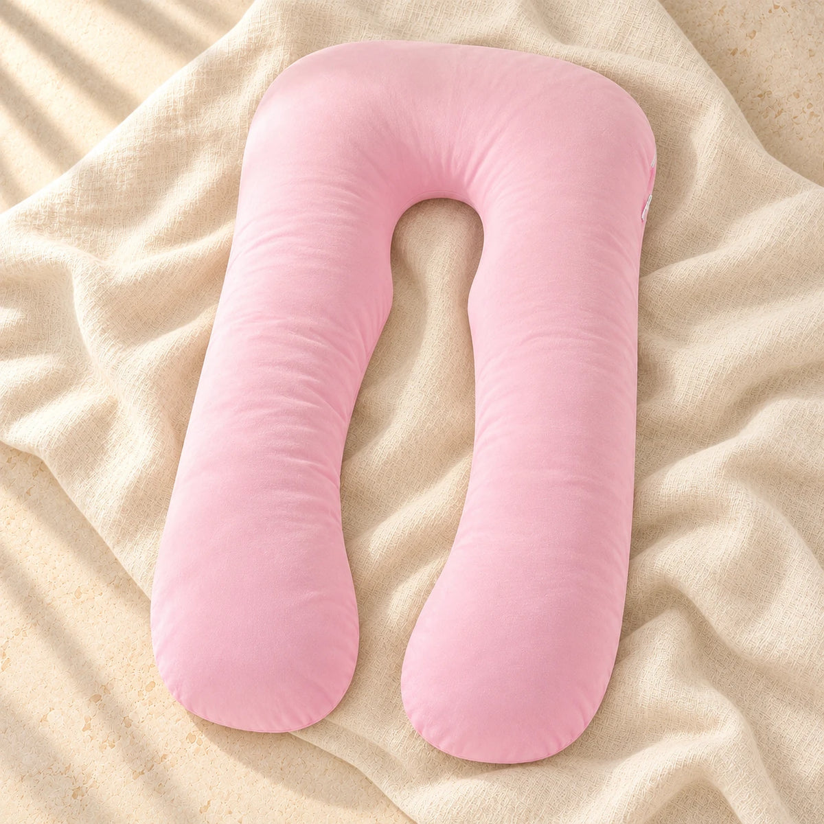 Pink U-shaped pregnancy pillow on warm cream linen