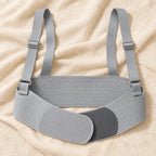 grey perforated under-bump support belt with wide back section, overlapping rounded fastening panels and two adjustable shoulder straps with matching rectangular sliders, product on cream linen