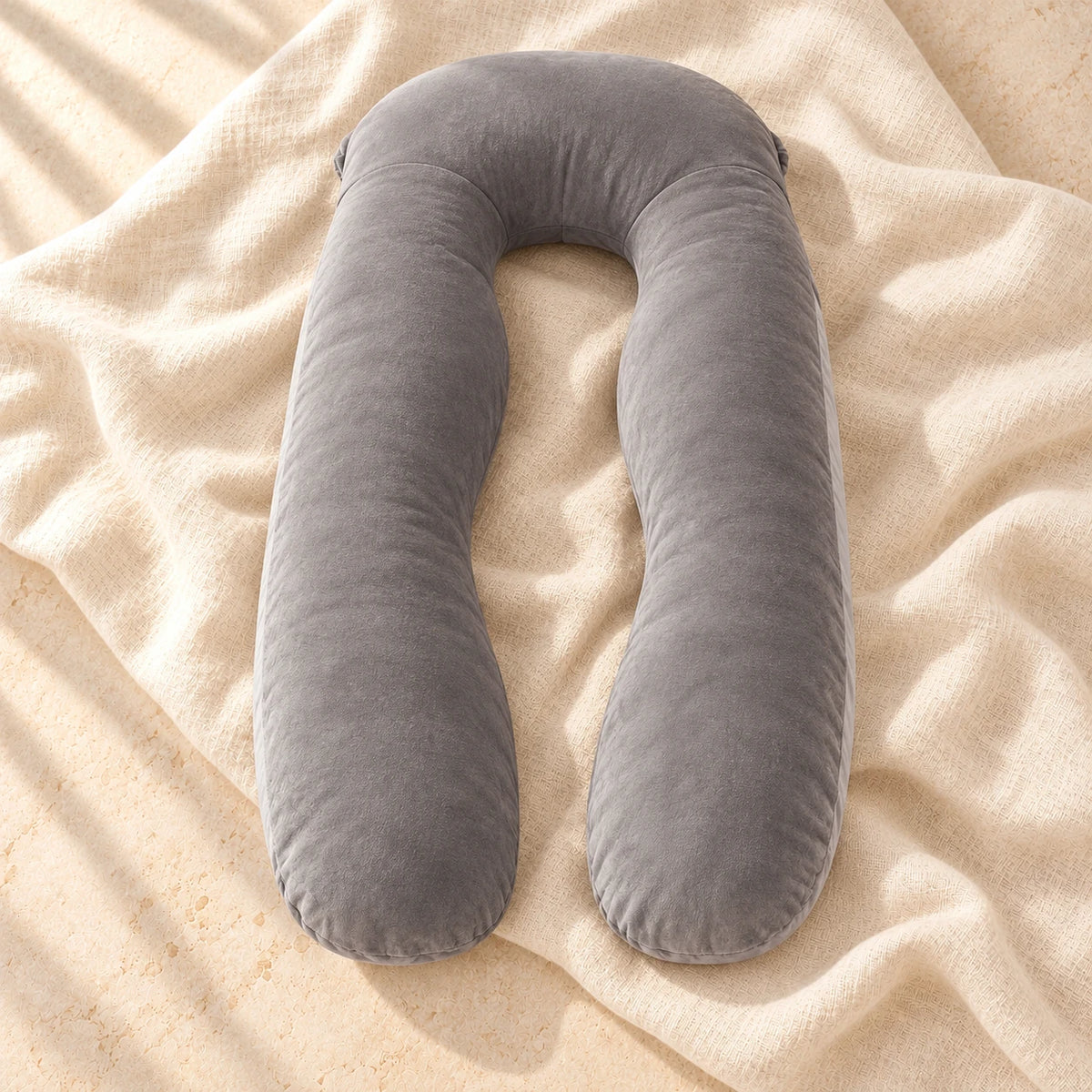 The grey U-shaped full-body pregnancy pillow photographed on warm cream linen