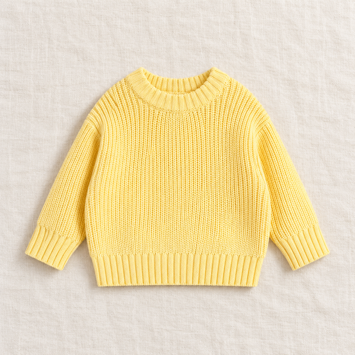 The Everyday Chunky Knit Sweater in Butter Yellow, laid flat on ivory linen