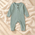 Muted sage green ribbed baby romper on warm ivory linen