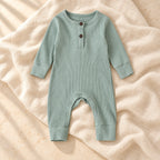 Muted sage green ribbed baby romper on warm ivory linen