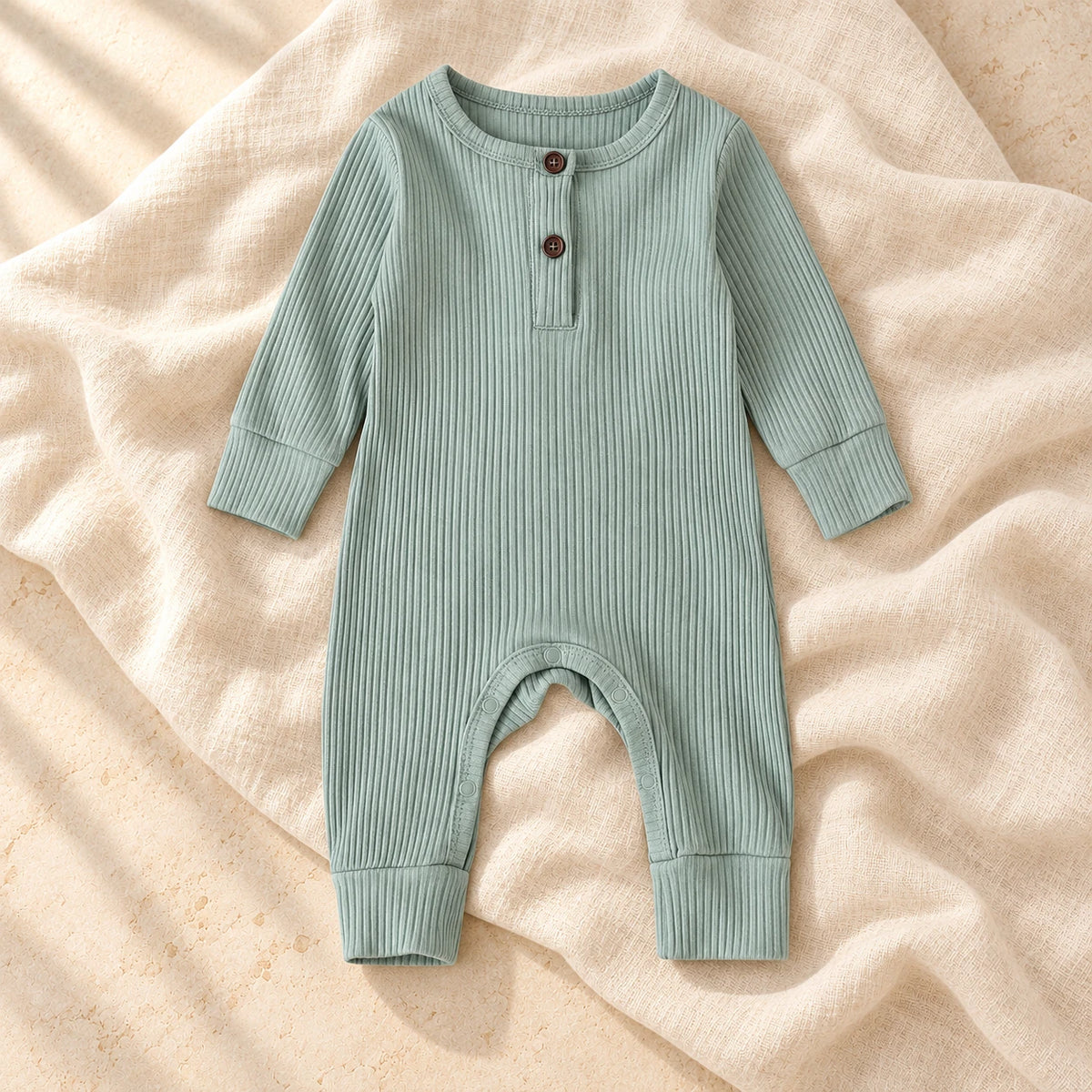Muted sage green ribbed baby romper on warm ivory linen