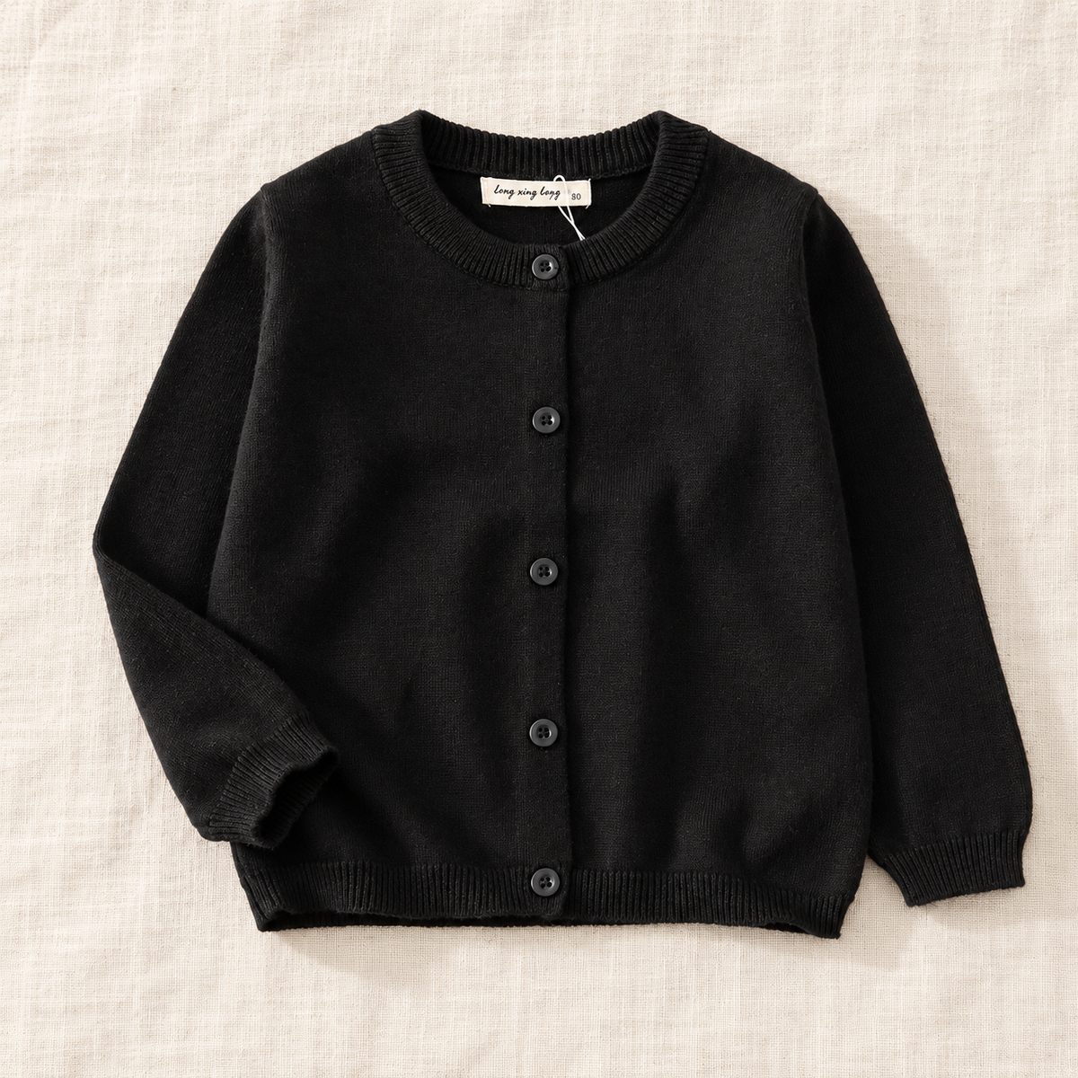 The Simple Button Knit Cardigan — Black, laid flat on ivory linen