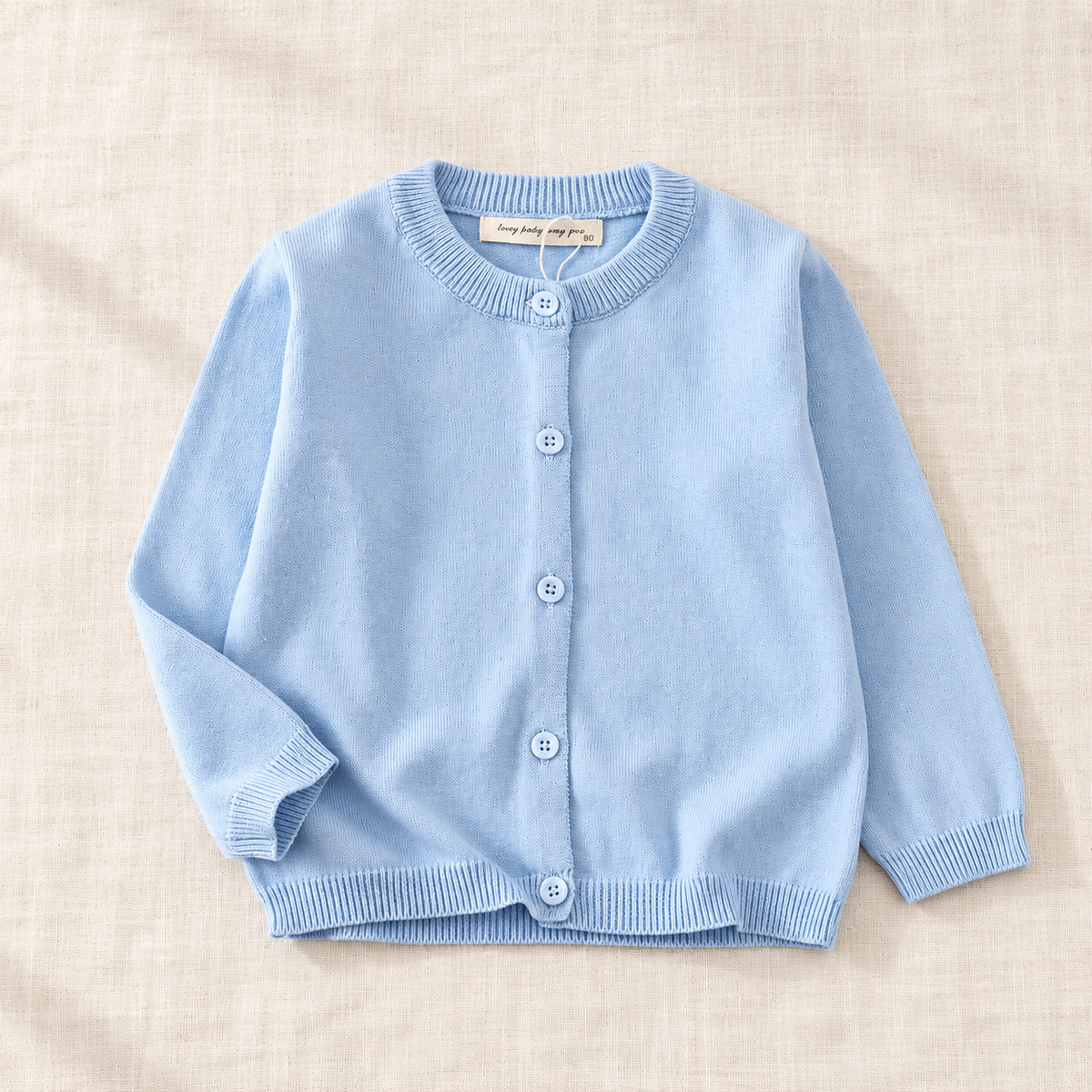The Simple Button Knit Cardigan — Light Blue, laid flat on ivory linen