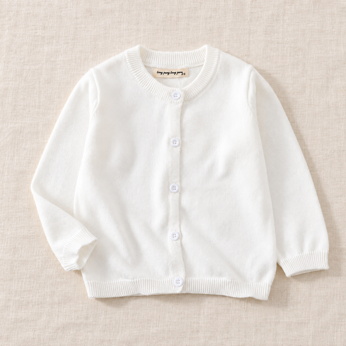 The Simple Button Knit Cardigan — White, laid flat on ivory linen