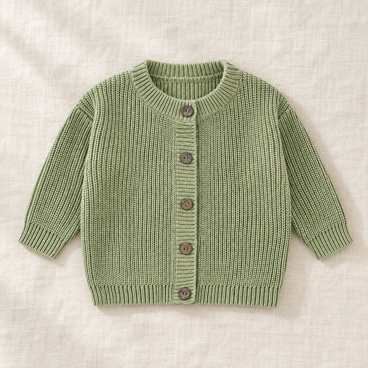 The Ribbed Button Knit Cardigan — Pea Green, laid flat on ivory linen