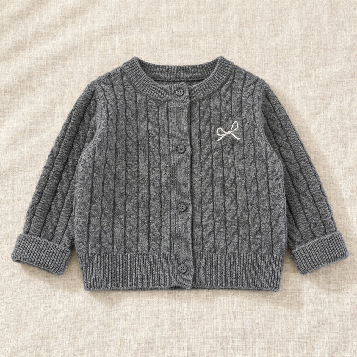 The Soft Cable Knit Cardigan — Gray, laid flat on ivory linen